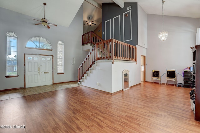 entryway with high vaulted ceiling, ceiling fan with notable chandelier, wood finished floors, baseboards, and stairs