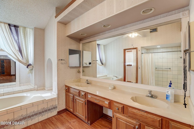 bathroom with wallpapered walls, a textured ceiling, a sink, and wood finished floors