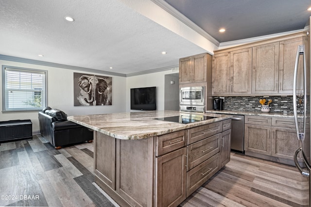 kitchen featuring light hardwood / wood-style floors, a textured ceiling, light stone countertops, a spacious island, and appliances with stainless steel finishes