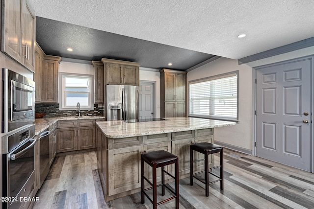 kitchen with stainless steel appliances, a textured ceiling, a center island, and light hardwood / wood-style flooring