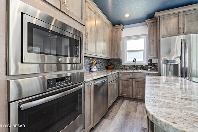 kitchen with light stone counters, appliances with stainless steel finishes, a textured ceiling, decorative backsplash, and light hardwood / wood-style floors