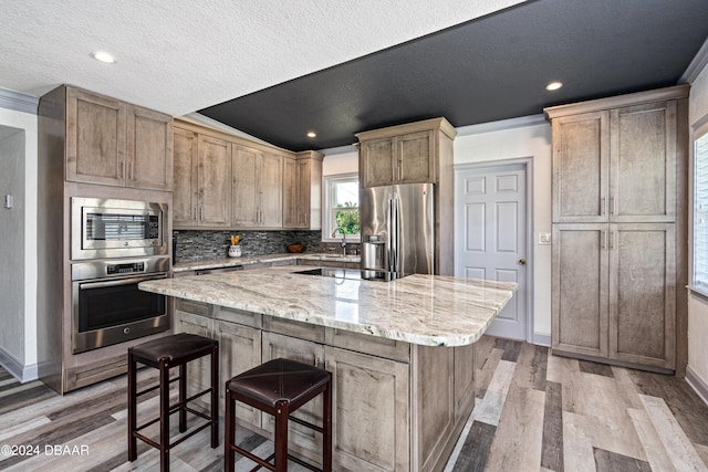 kitchen with stainless steel appliances, light stone counters, ornamental molding, light hardwood / wood-style flooring, and a kitchen island