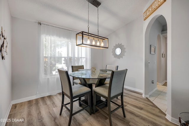 dining space featuring baseboards, arched walkways, a textured ceiling, and light wood finished floors