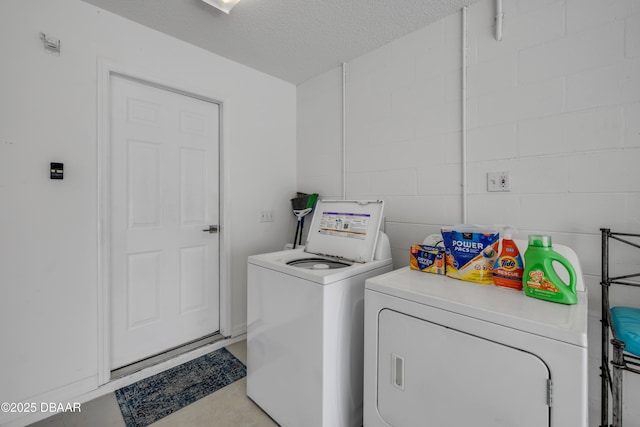 washroom featuring a textured ceiling, concrete block wall, laundry area, and washer and clothes dryer