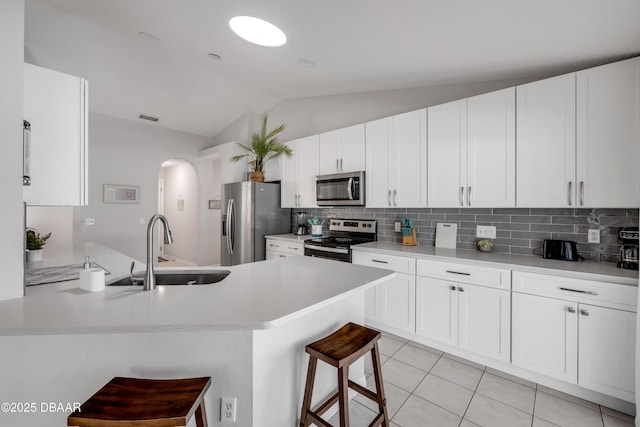 kitchen featuring a kitchen breakfast bar, light tile patterned flooring, arched walkways, stainless steel appliances, and a sink