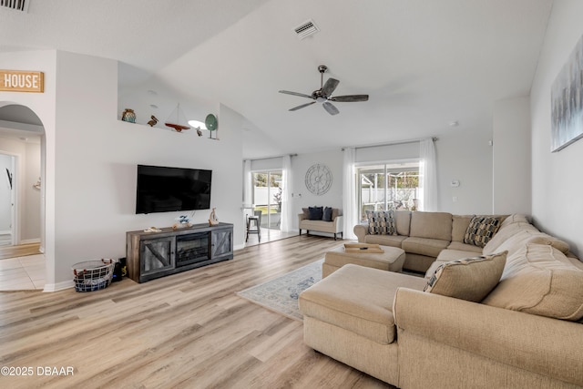 living room featuring a ceiling fan, baseboards, lofted ceiling, arched walkways, and light wood-style floors