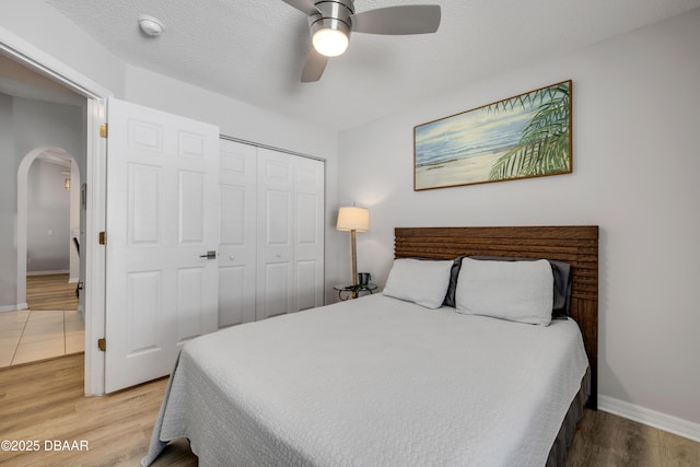 bedroom with arched walkways, a textured ceiling, light wood-type flooring, and a closet