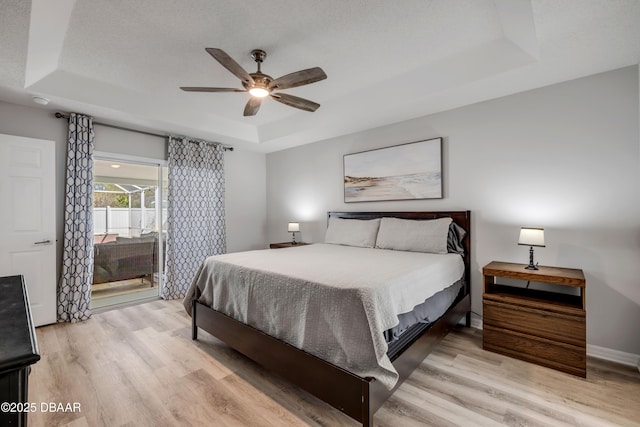 bedroom with light wood finished floors, baseboards, a tray ceiling, and a ceiling fan