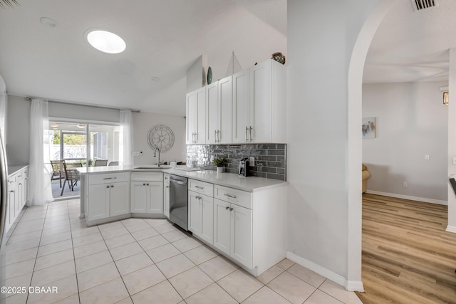 kitchen with backsplash, a peninsula, stainless steel dishwasher, arched walkways, and a sink