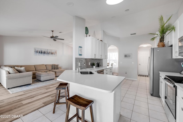 kitchen featuring electric range, a ceiling fan, a sink, arched walkways, and lofted ceiling