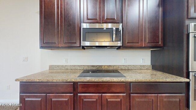 kitchen with light stone countertops, stainless steel microwave, black electric cooktop, and refrigerator