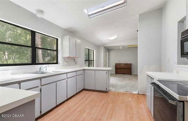 kitchen featuring sink, kitchen peninsula, vaulted ceiling with skylight, light hardwood / wood-style flooring, and electric range