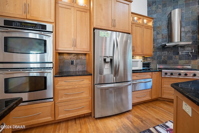 kitchen featuring light hardwood / wood-style flooring, dark stone counters, wall chimney range hood, and stainless steel appliances