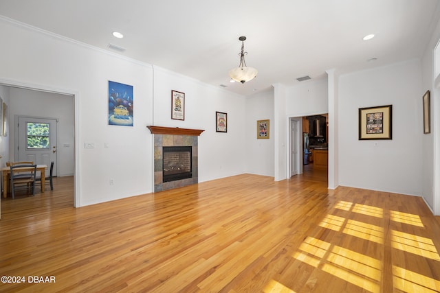 living room featuring a tile fireplace, light hardwood / wood-style floors, and crown molding