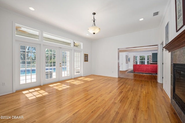 unfurnished living room featuring ornamental molding, french doors, light hardwood / wood-style floors, and a fireplace