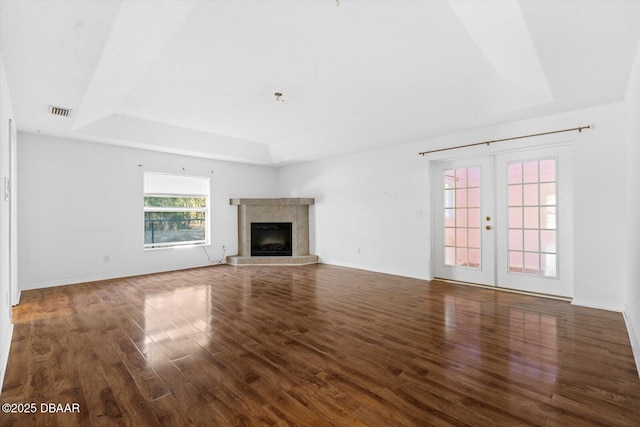 unfurnished living room with a raised ceiling, a tile fireplace, french doors, and dark hardwood / wood-style floors