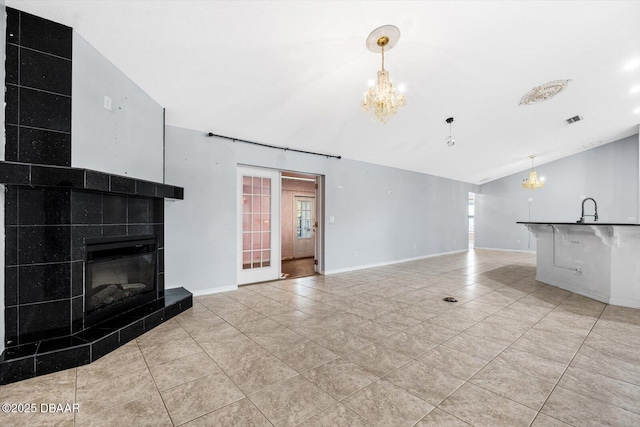 unfurnished living room featuring a fireplace, light tile patterned flooring, vaulted ceiling, and an inviting chandelier