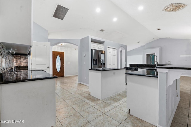 kitchen with a kitchen island, white cabinetry, stainless steel refrigerator with ice dispenser, and vaulted ceiling