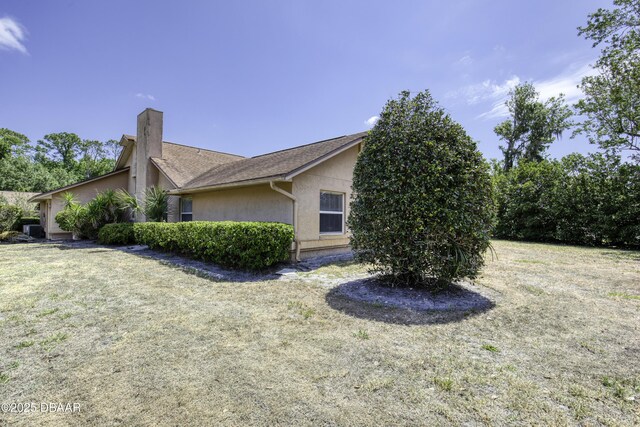 view of side of property with a yard, a chimney, and stucco siding