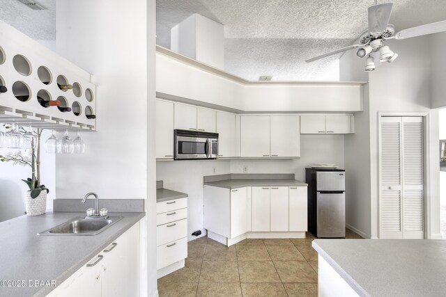 kitchen with ceiling fan, appliances with stainless steel finishes, a sink, light tile patterned floors, and a high ceiling
