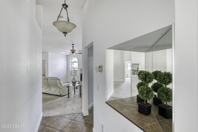 hallway with carpet flooring, a textured ceiling, baseboards, and tile patterned floors