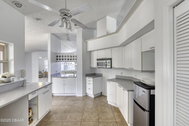 kitchen with ceiling fan, a sink, a textured ceiling, stainless steel appliances, and white cabinetry