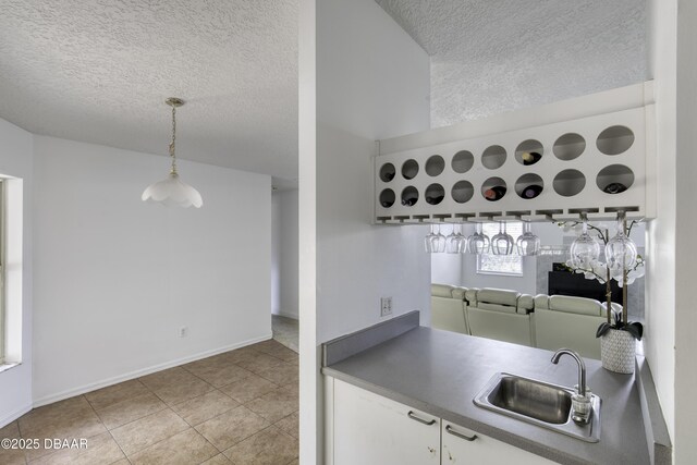 kitchen with a sink, a textured ceiling, tile patterned floors, decorative light fixtures, and baseboards