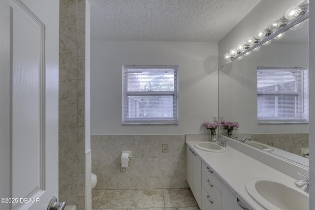 bathroom featuring a sink, a textured ceiling, toilet, and tile walls