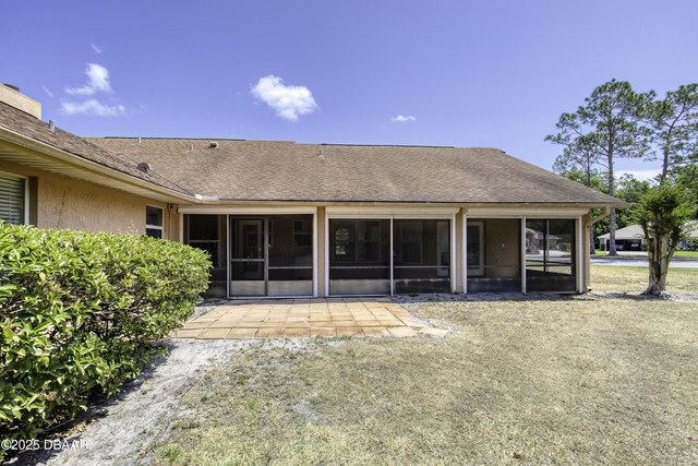 back of property with a shingled roof, a sunroom, and a patio area