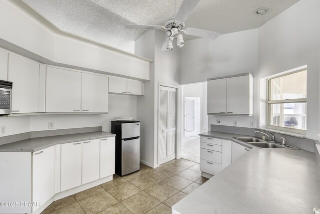 kitchen featuring a ceiling fan, a textured ceiling, a sink, high vaulted ceiling, and freestanding refrigerator