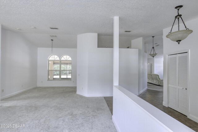 empty room featuring a textured ceiling, vaulted ceiling, baseboards, and carpet