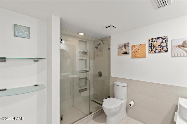 bathroom with tile patterned floors, toilet, a shower with door, tile walls, and vanity