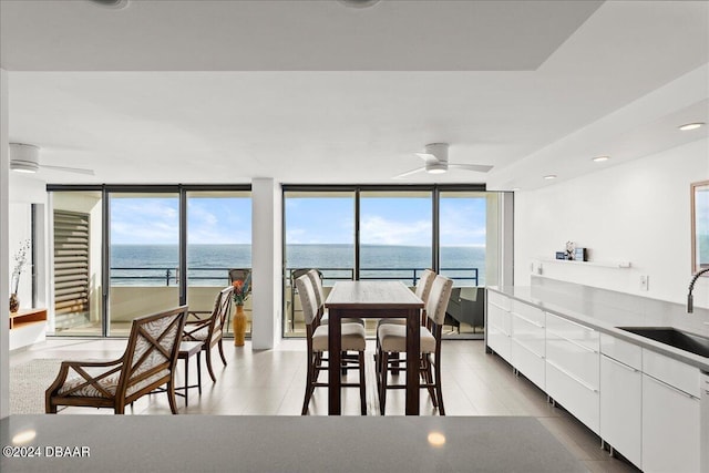 dining room featuring expansive windows, ceiling fan, sink, and a water view