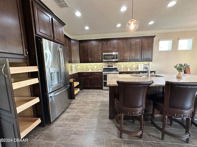 kitchen with ornamental molding, dark brown cabinetry, stainless steel appliances, sink, and hanging light fixtures