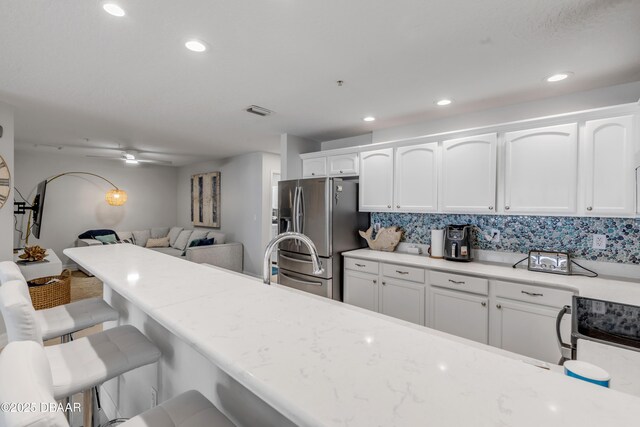 kitchen featuring stainless steel refrigerator with ice dispenser, white cabinetry, and a breakfast bar area