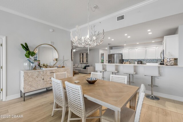 dining area with crown molding, an inviting chandelier, and light hardwood / wood-style flooring