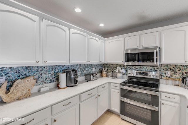 kitchen featuring appliances with stainless steel finishes, light tile patterned floors, white cabinets, and decorative backsplash