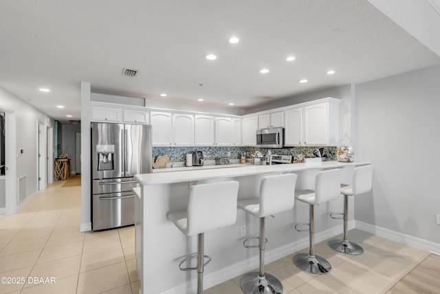 kitchen featuring stainless steel appliances, a breakfast bar, light tile patterned floors, and white cabinets