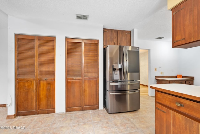 1 River Bluff Ct, Ormond Beach, FL 32174 - kitchen featuring stainless steel fridge with ice dispenser, a textured ceiling, light tile patterned flooring, light countertops, and brown cabinetry