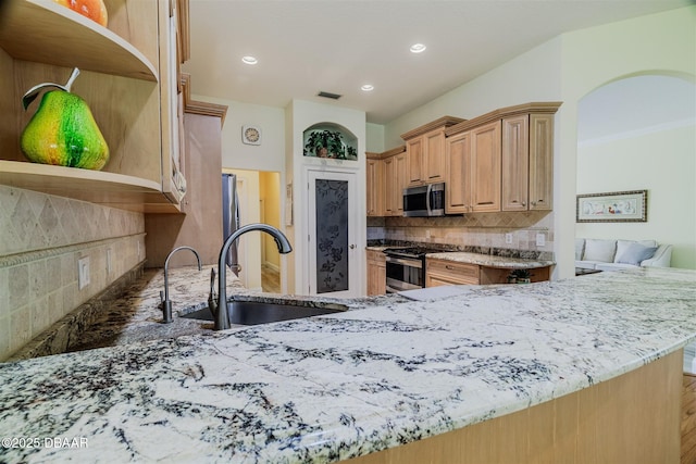 kitchen with sink, light stone counters, appliances with stainless steel finishes, kitchen peninsula, and backsplash