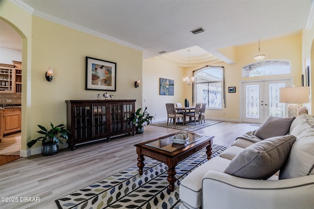 living room featuring crown molding, light hardwood / wood-style flooring, french doors, and a textured ceiling