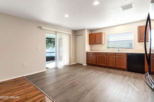 kitchen featuring sink, a textured ceiling, black dishwasher, and light wood-type flooring