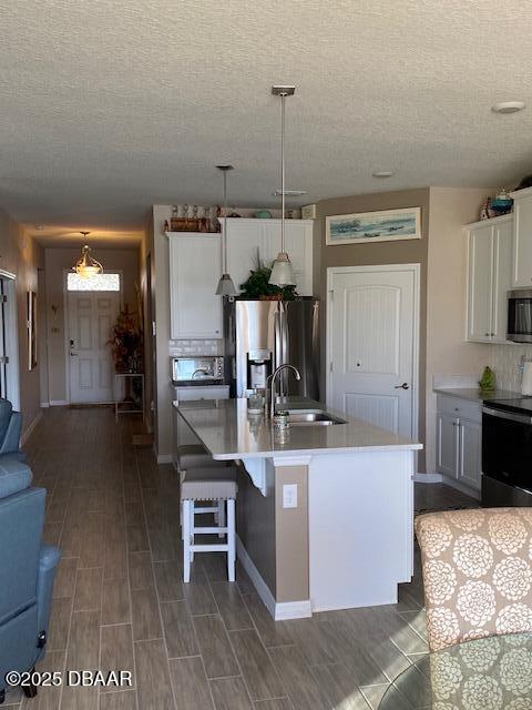 kitchen featuring a sink, white cabinets, light countertops, appliances with stainless steel finishes, and an island with sink