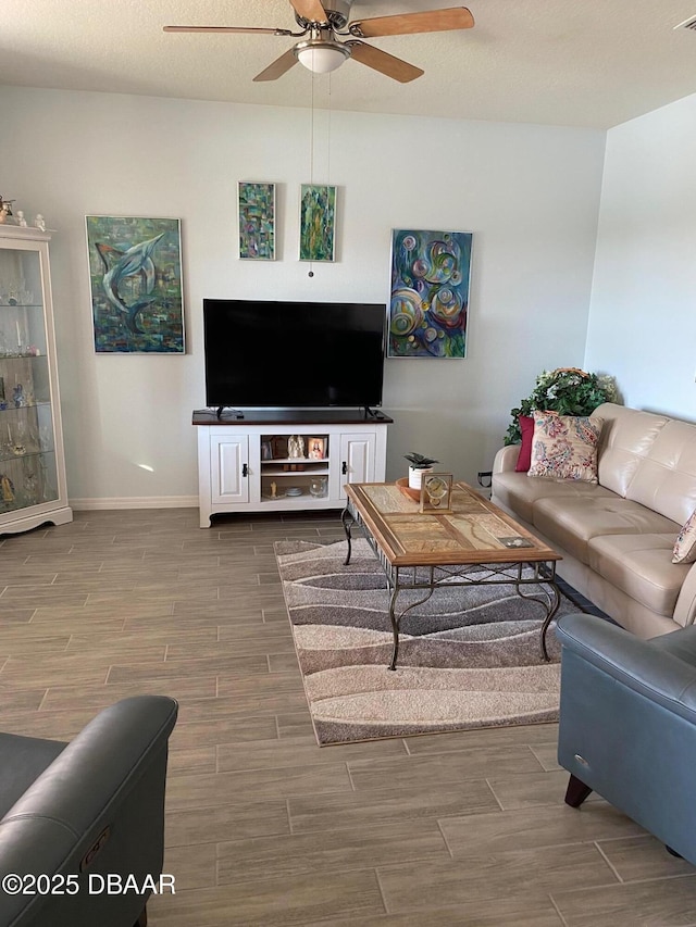 living room featuring ceiling fan, baseboards, a textured ceiling, and wood finish floors