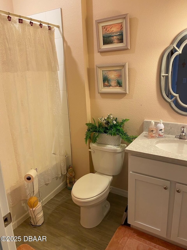 bathroom featuring baseboards, toilet, wood finished floors, shower / bathtub combination with curtain, and vanity