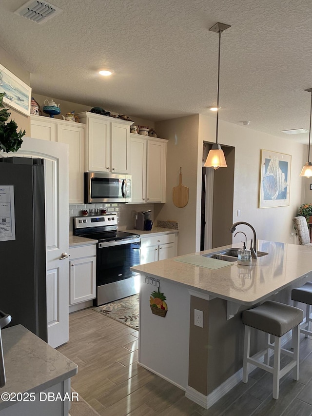 1601 Delphi Way, New Smyrna Beach, FL 32168 - kitchen with stainless steel appliances, light wood-type flooring, white cabinets, decorative light fixtures, and a textured ceiling