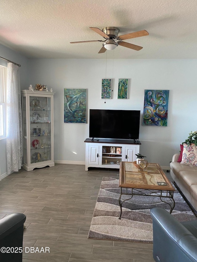 living area with ceiling fan, wood finish floors, a textured ceiling, and baseboards