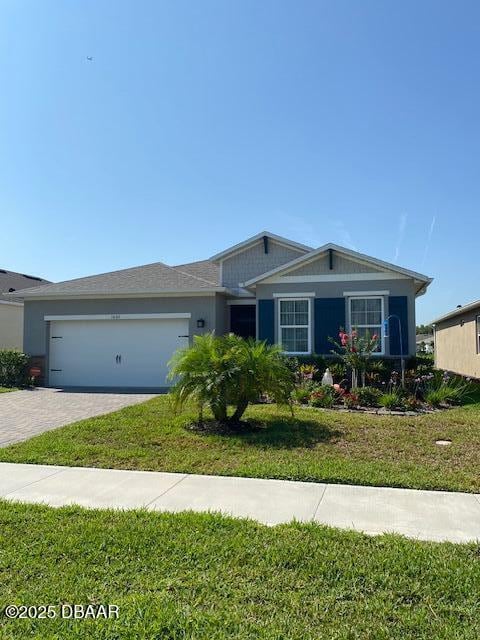 single story home featuring a front yard, decorative driveway, and an attached garage