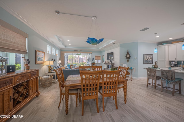 dining room with a raised ceiling, light wood-type flooring, plenty of natural light, and ornamental molding