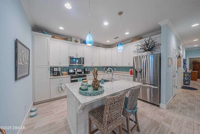 kitchen featuring a center island with sink, sink, white cabinetry, hanging light fixtures, and stainless steel appliances